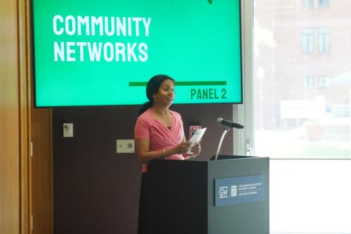 Elizabeth Chacko speaking at a podium in front of a presentation slide labeled "Community Networks"